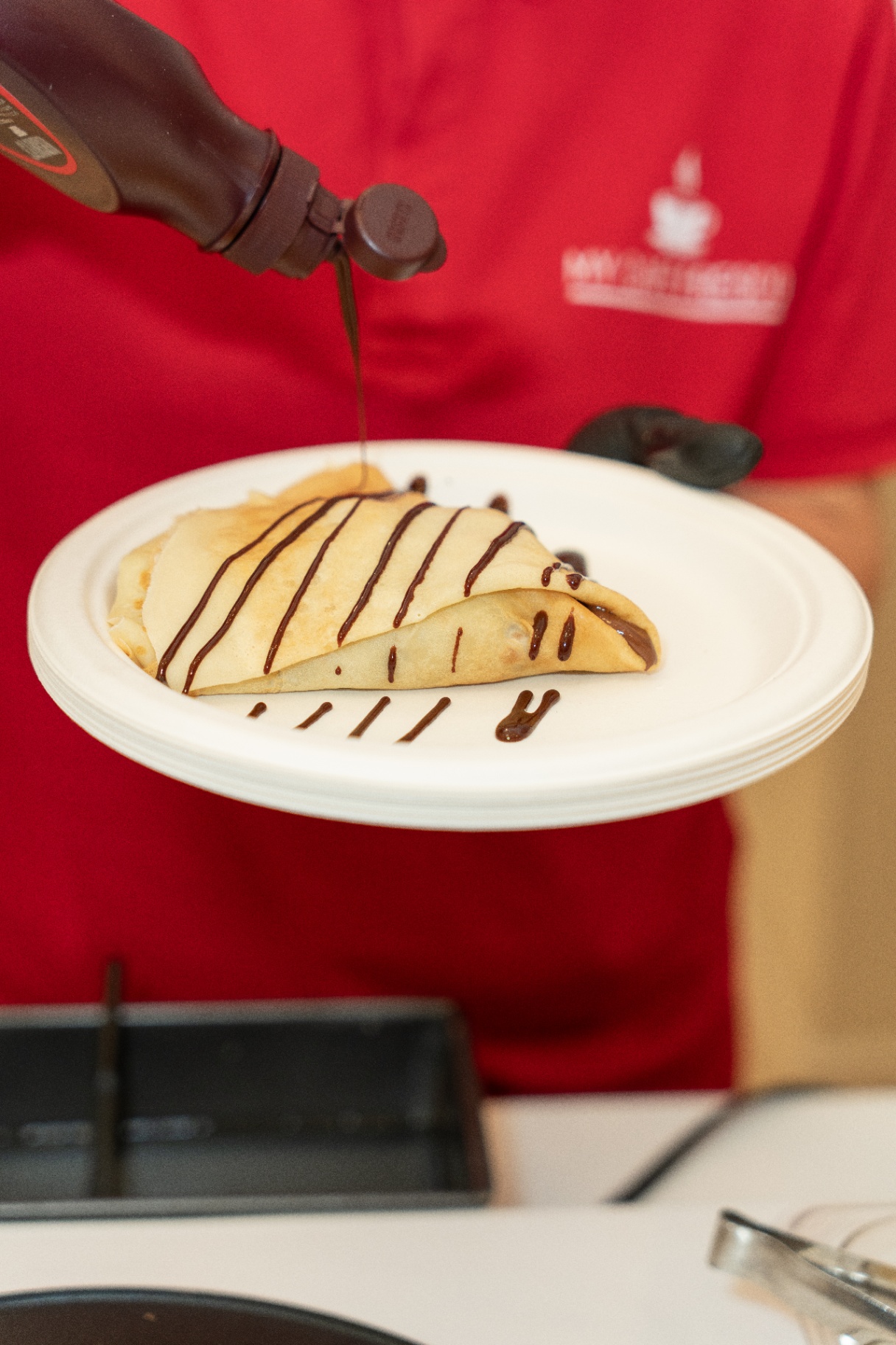 Chocolate sauce being poured over a fresh crepe