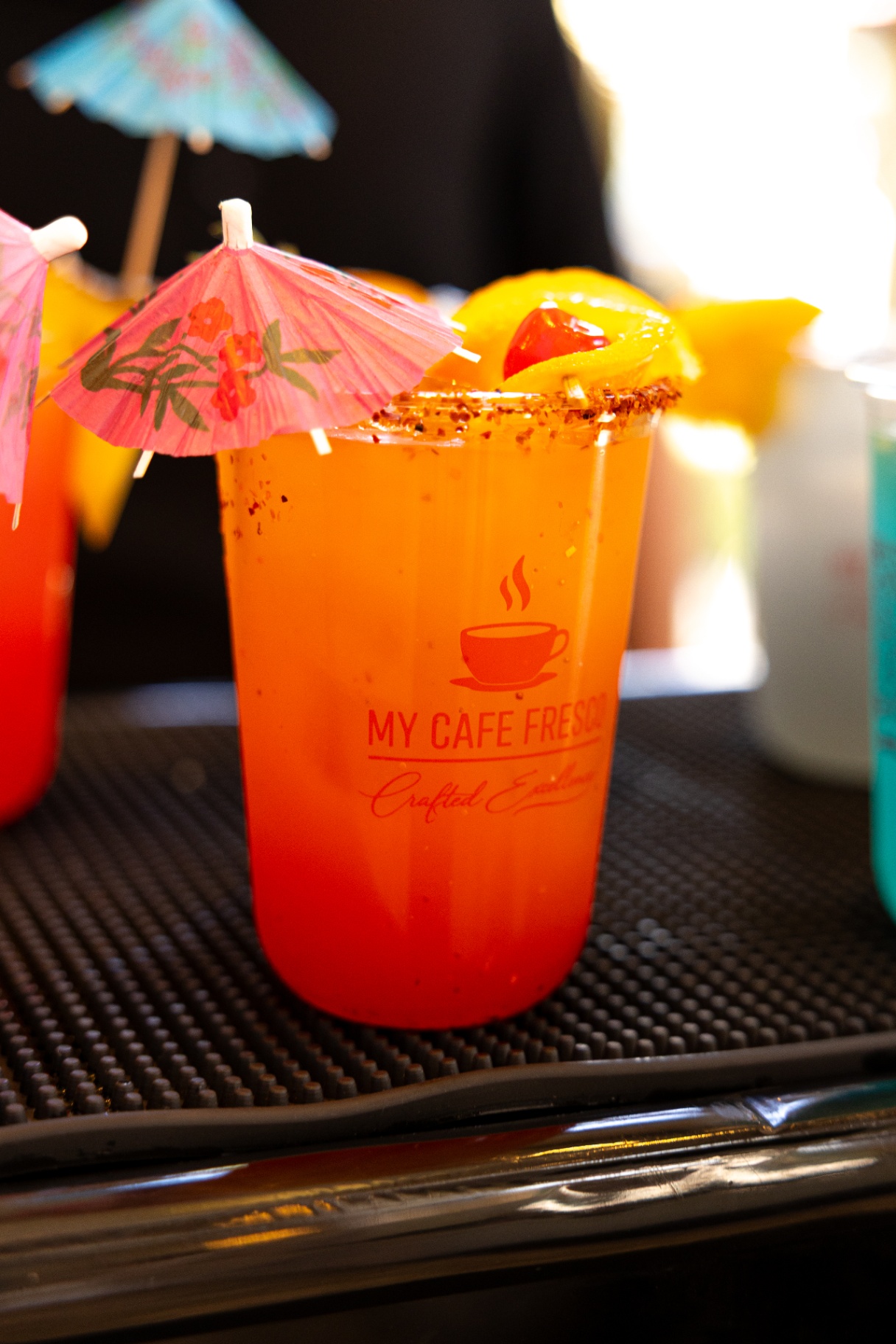 Sunrise mocktail with tajin rim, cherry, and paper umbrella