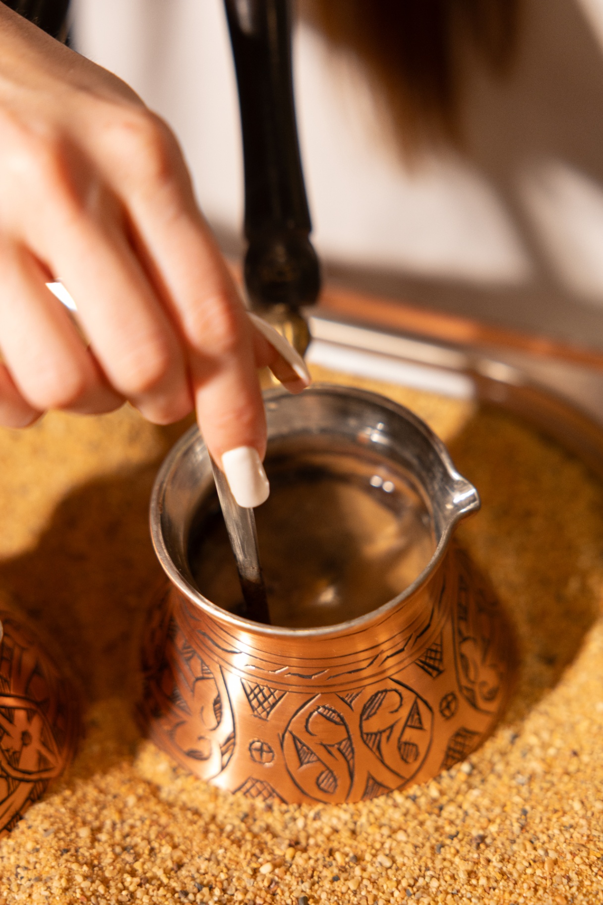 Armenian coffee being stirred in a copper jazzve nestled in hot sand